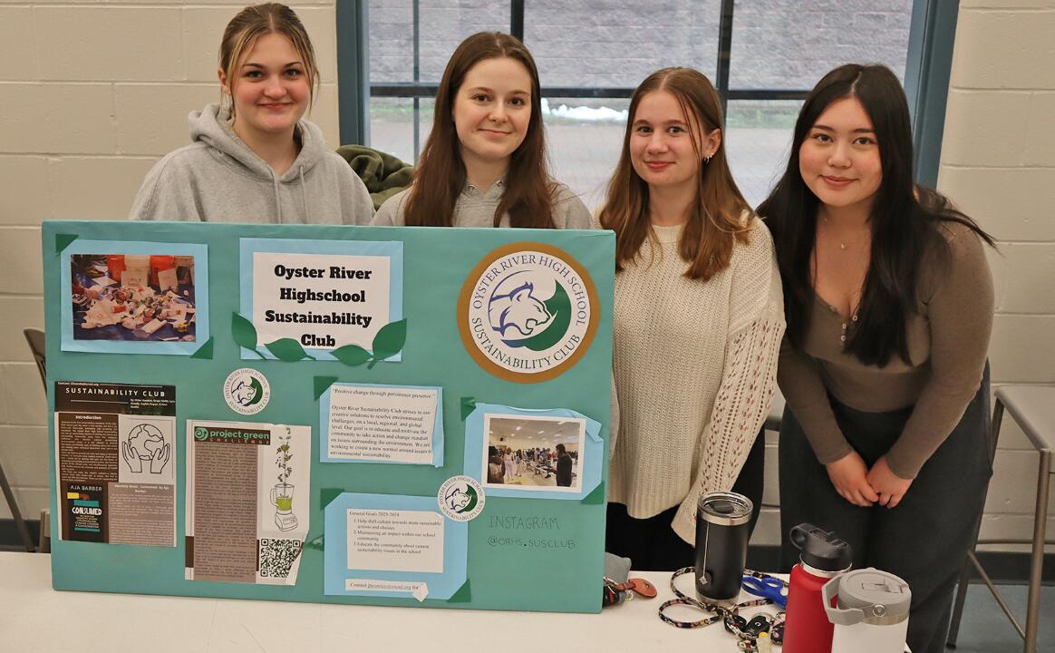 Four members of the high school sustainability club at a table with informational poster.