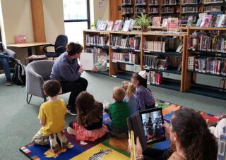 A photo of Oyster River nurse Kim Wolph reading to pre-k students in a library.