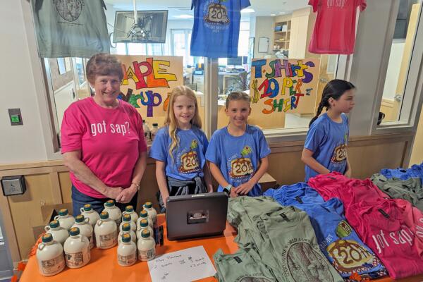 An adult and three Moharimet students operating the t-shirt and maple syrup stand.