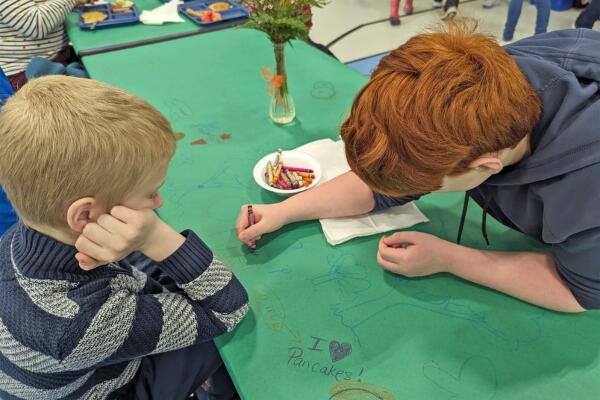 Two Oyster River students drawing on the tablecloth with crayons during the pancake breakfast.