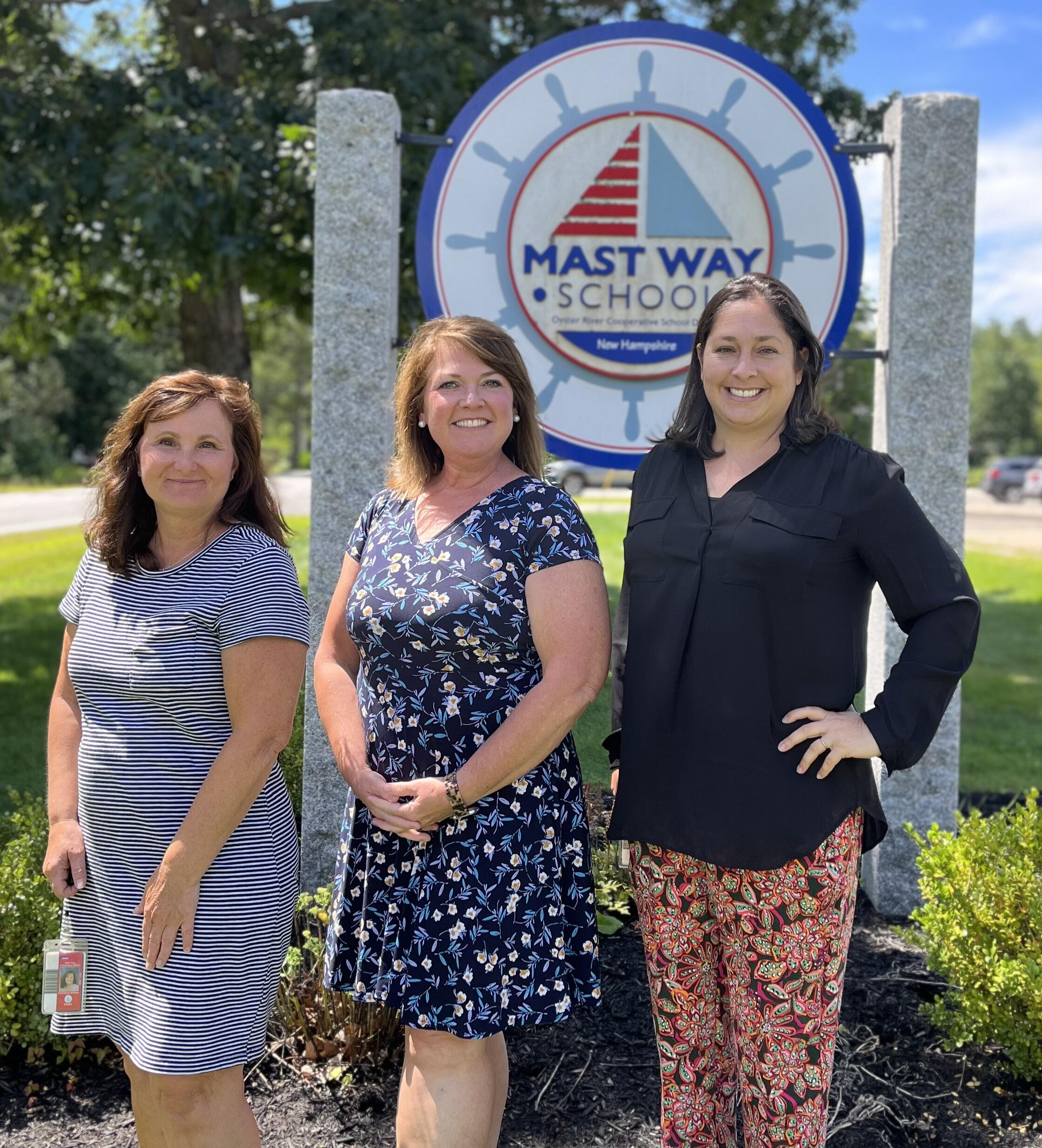 A photograph of Assistant to the Principal Christine Nelson, Principal Misty Lowe, and Secretary Devon Anthony taken outside Mast Way Elementary School in front of the school's logo.