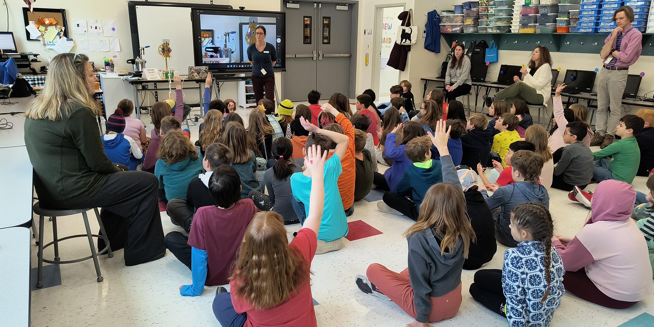 A photo of Mast Way's 4th grade students with raised hands in a classroom