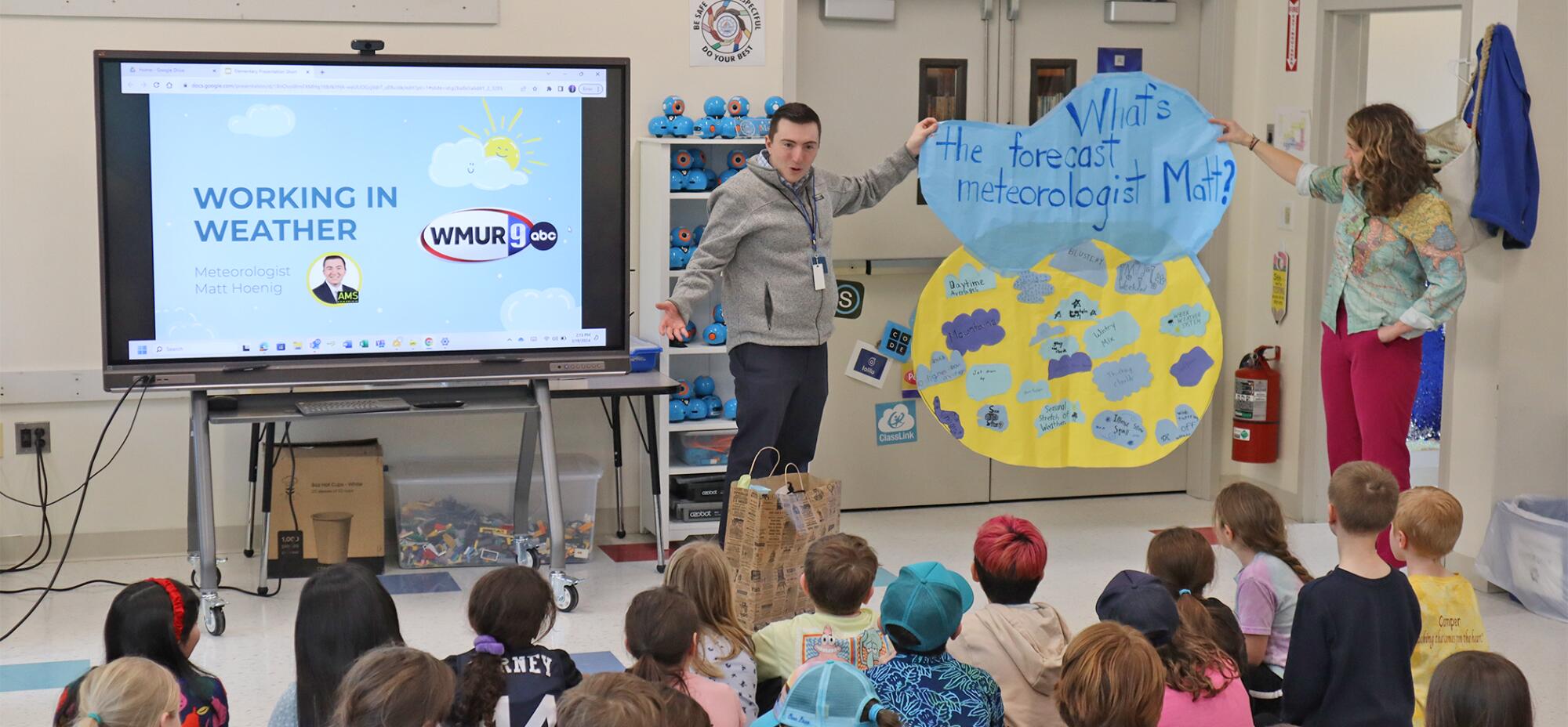 Meteorologist Matt Hoenig holds up a handmade weather cloud sign while presenting to a room full of students.